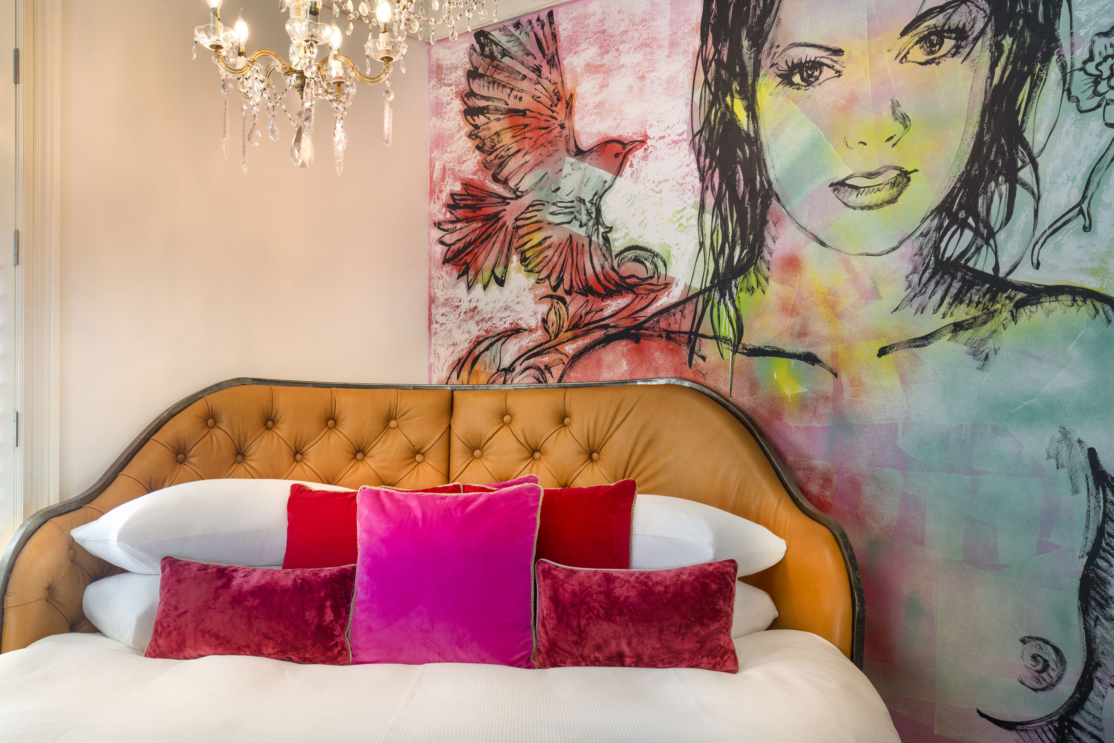 Un dormitorio con un cabecero capitonado, una cama con almohadas blancas y rojas, y un cuadro abstracto grande en la pared.