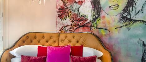 A bedroom with a tufted headboard, a bed with white and red pillows, and a large abstract painting on the wall.