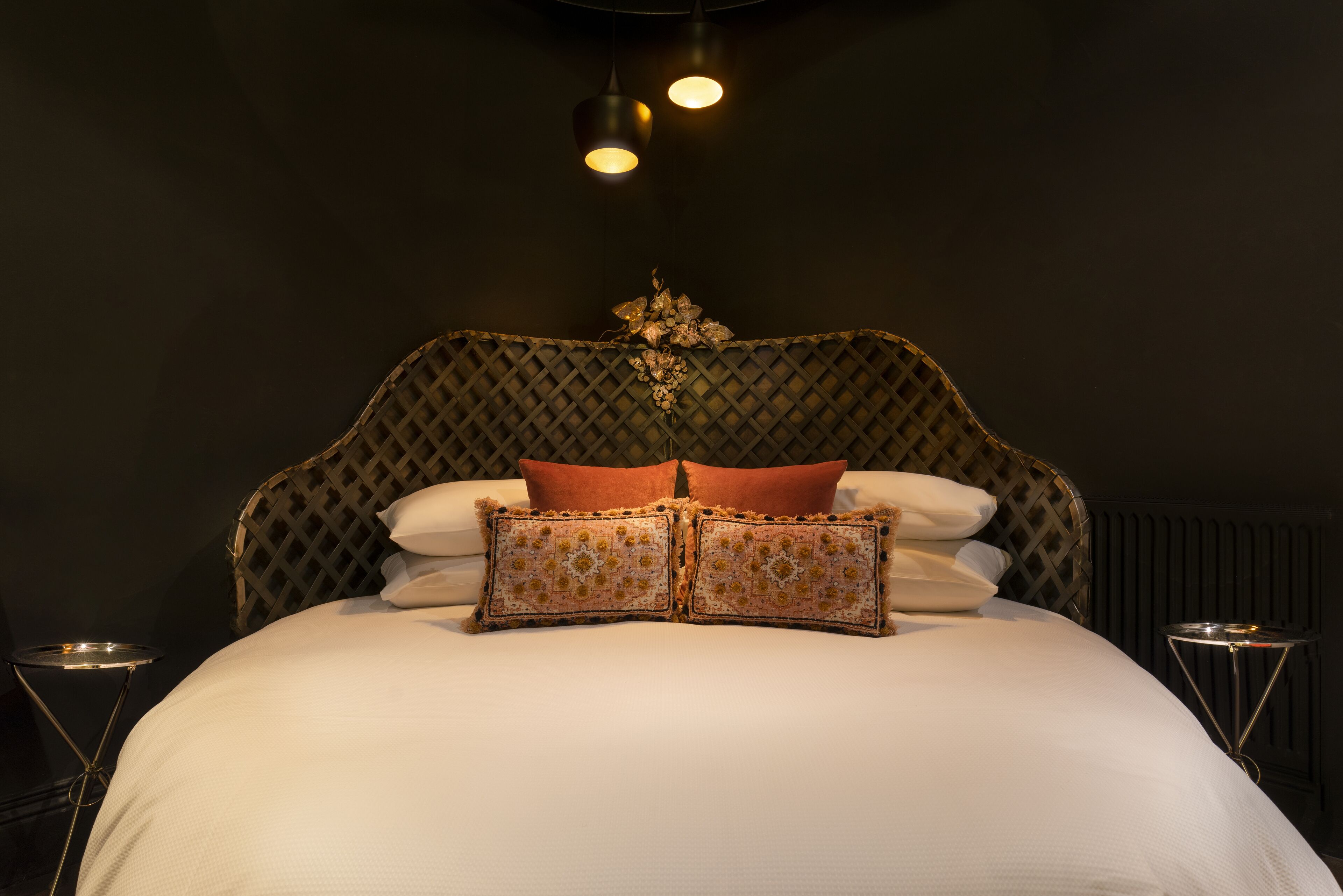 A neatly made bed with a patterned headboard, two bedside tables, and a decorative wall hanging.