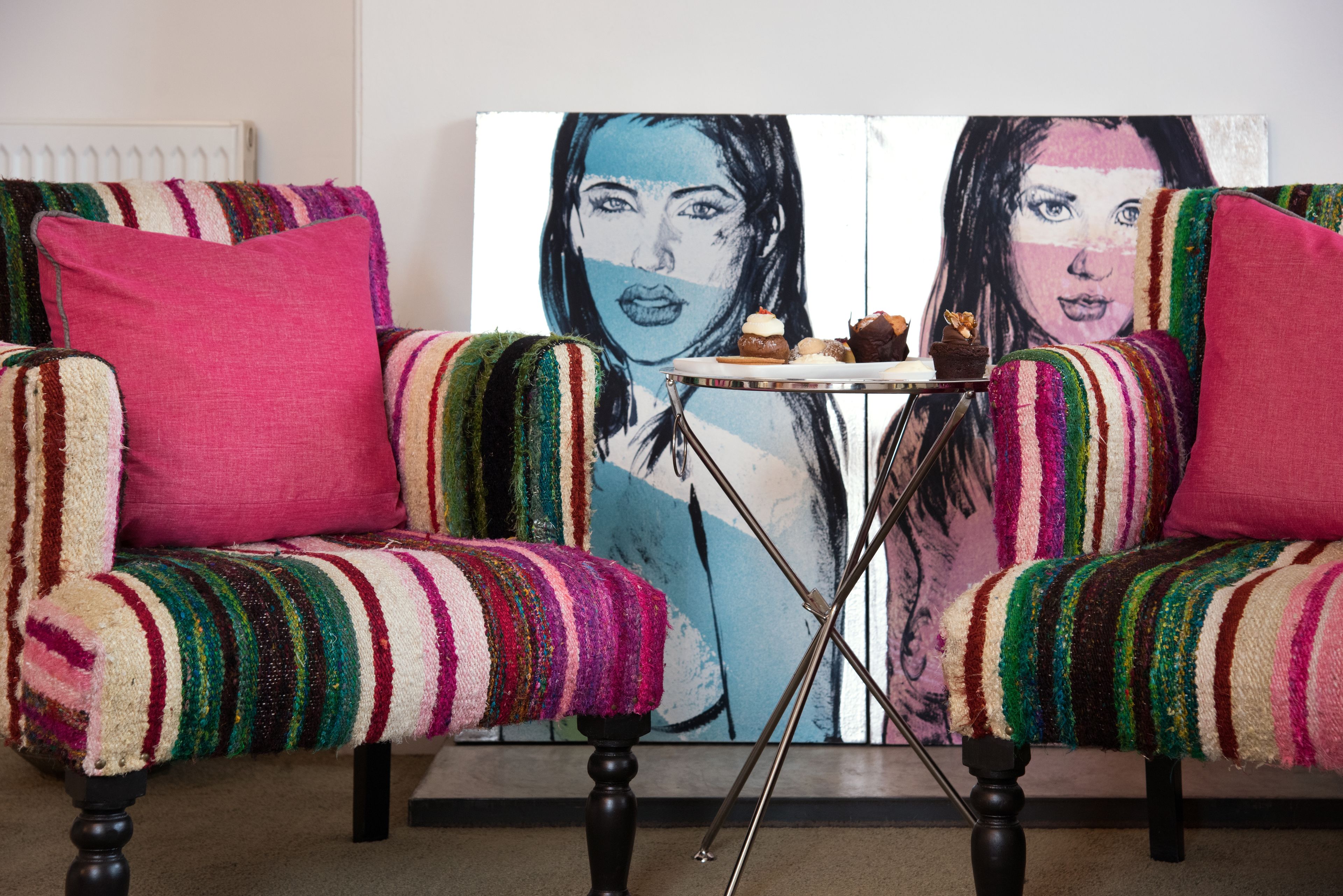A room with two upholstered armchairs with colorful striped upholstery, a small table with a plate of food, and a large painting on the wall.