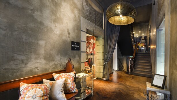 A reception area with a wooden bench, patterned pillows, a reception desk, and a staircase leading to an upper level. - Hotel Frangos (Daylesford)