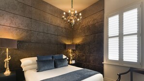 A bedroom with a large bed, two bedside tables with lamps, a chandelier, and a window with blinds. - Hotel Frangos (Daylesford)