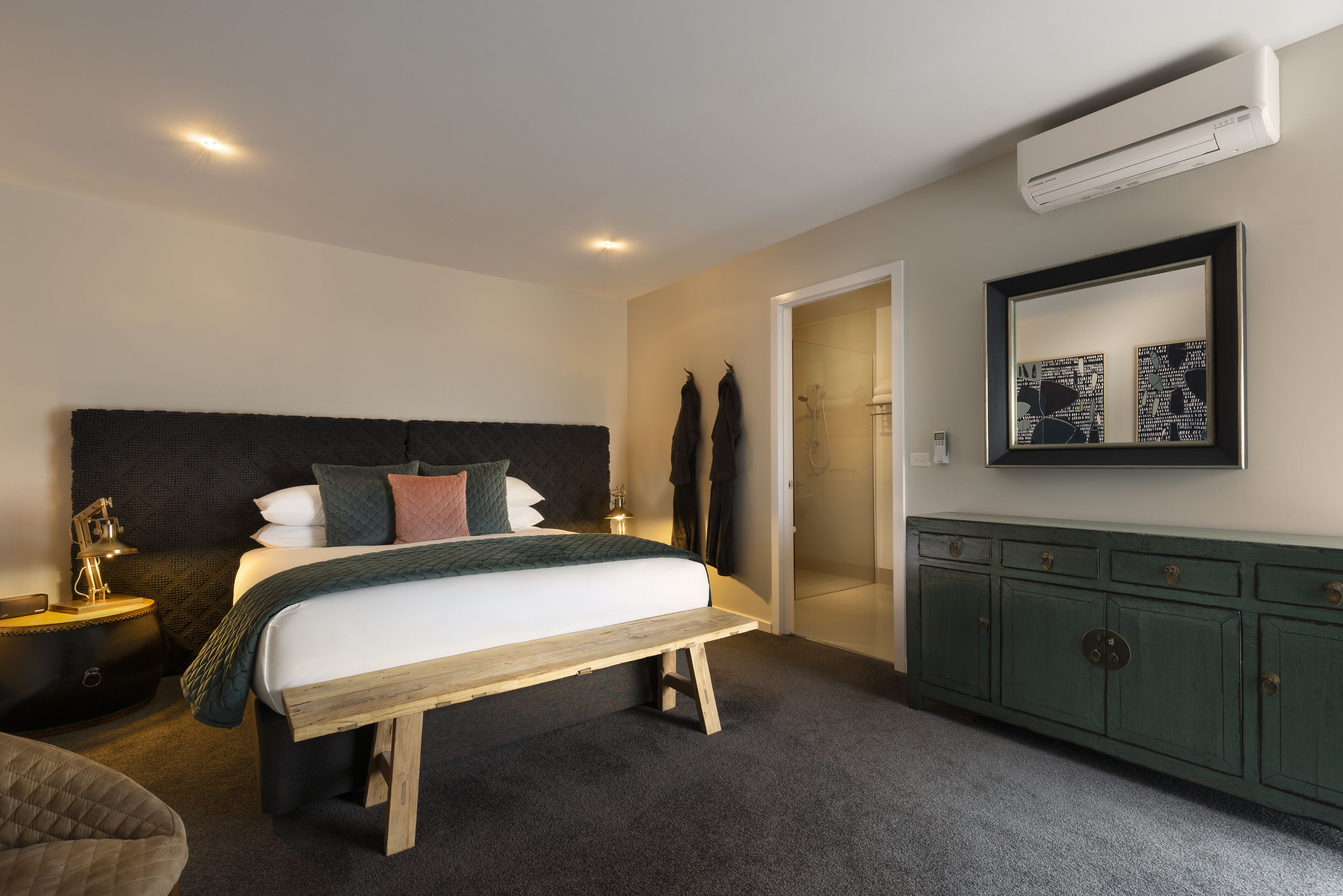 Een slaapkamer met een bed, nachtkastjes, een bankje, een garderobe en een spiegel.
