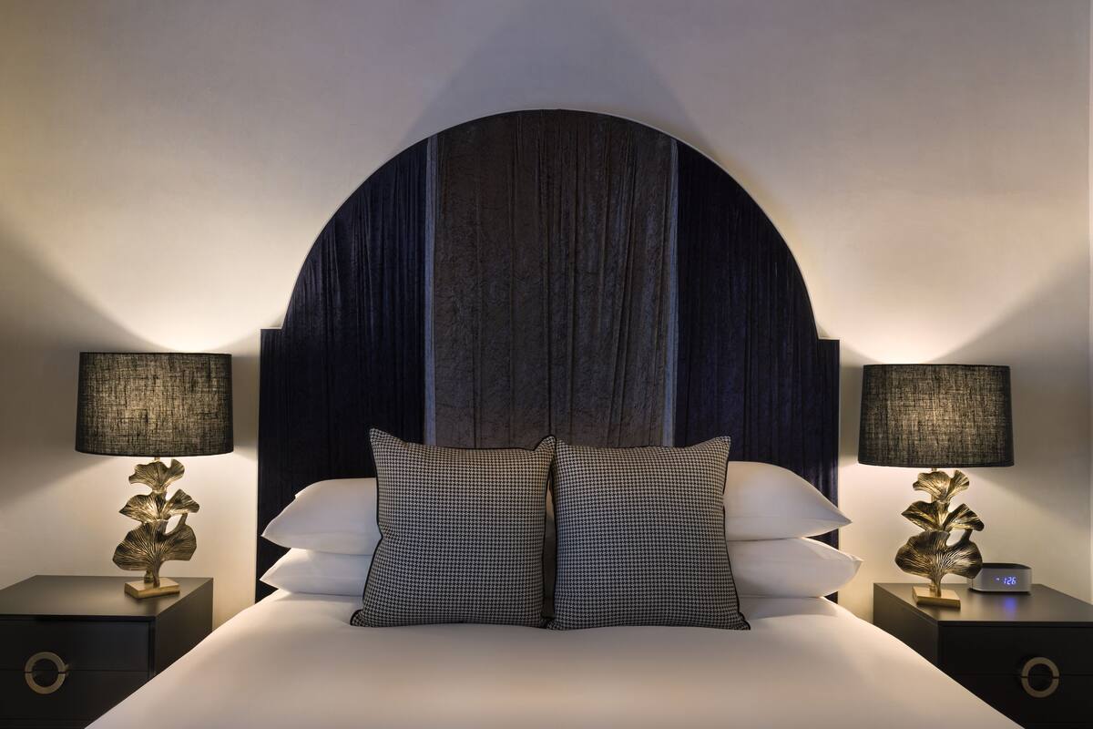 A neatly made bed with two matching pillows, flanked by two nightstands with lamps and clocks.