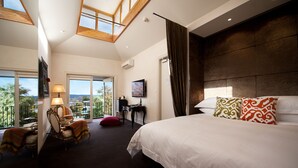 A hotel room with a large bed, a desk, a chair, a TV, and a balcony with a view. - Hotel Frangos (Daylesford)
