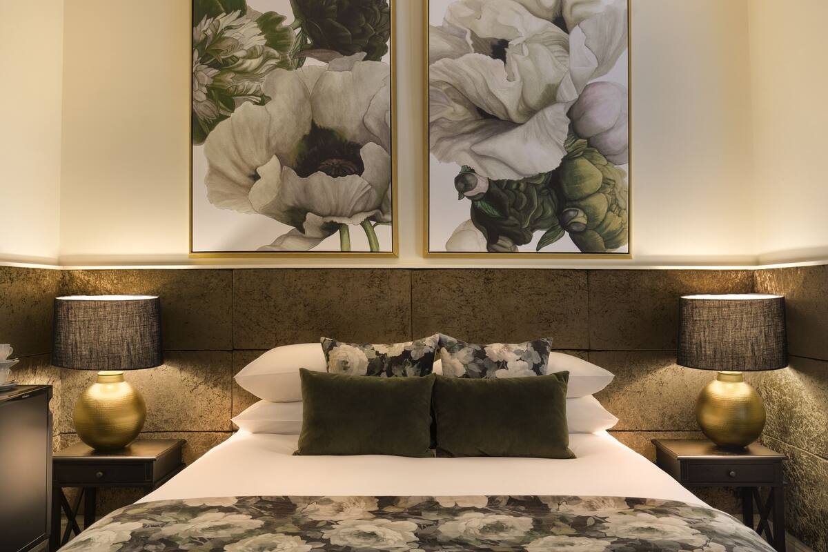 A neatly arranged bedroom with a large bed, two bedside tables with lamps, and two floral paintings on the wall.