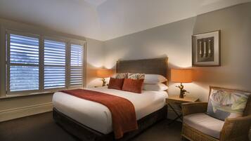 A neatly arranged bedroom with a large bed, two bedside lamps, a wicker chair, and a framed picture on the wall.