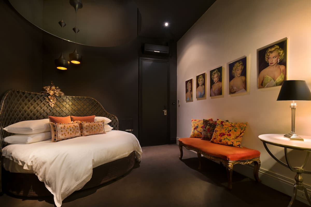 A bedroom with a bed, a bench, a round table, and wall art.