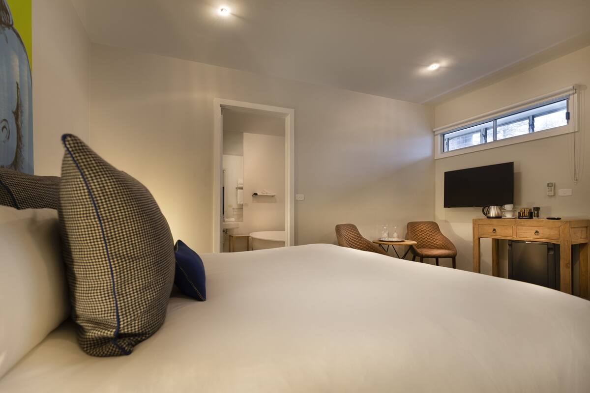 A hotel room with a large bed, a TV, a desk, and a chair.