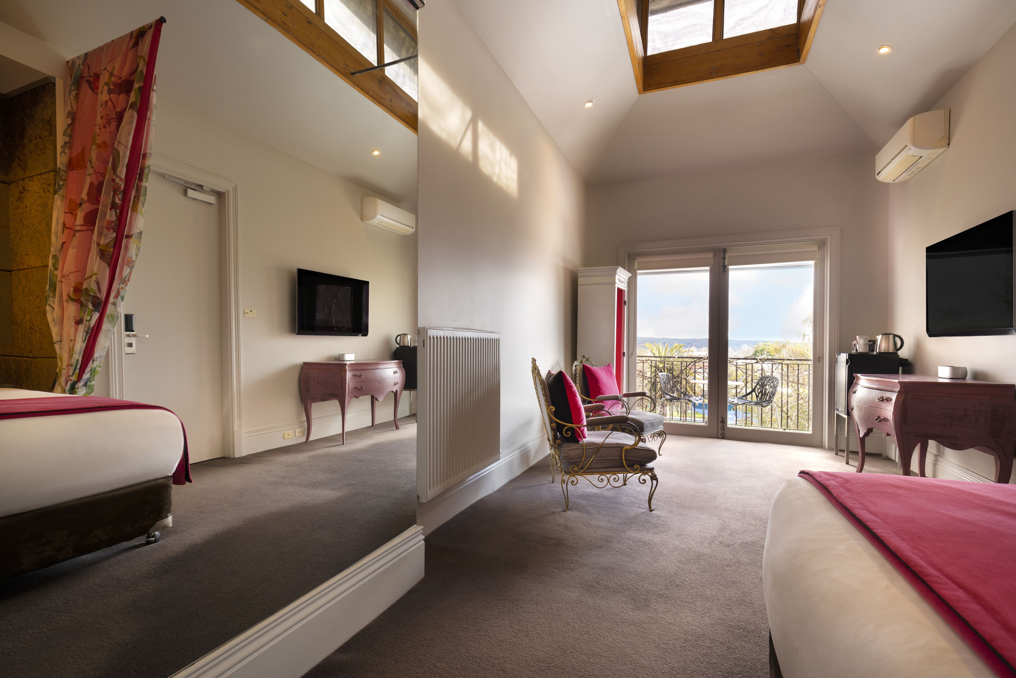 A hotel room with two beds, a television, a radiator, a balcony with a view, and a desk with a chair.