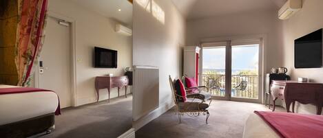 A hotel room with two beds, a television, a radiator, a balcony with a view, and a desk with a chair.