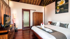 A hotel room with a bed, a wooden desk, a lamp, a painting, and a wardrobe. - Villa Keluarga (Lembongan Island)