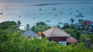 A coastal village with thatched-roof houses, a calm sea with boats, and lush greenery. - Villa Keluarga (Lembongan Island)