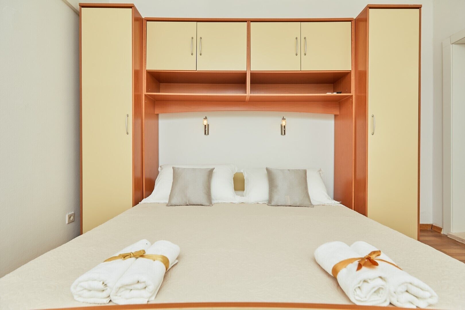 A hotel room with a bed, two wooden cabinets, and a headboard with two wall-mounted lights.