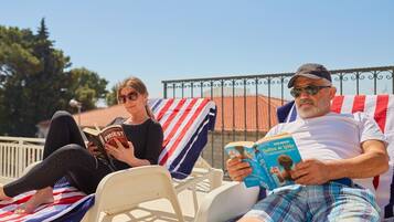Two people relaxing on sun loungers with striped towels, reading books.