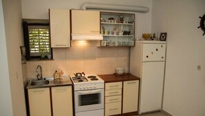 A compact kitchen with a stove, sink, and white refrigerator. - Villa Kate Dadic (Dubrovnik)