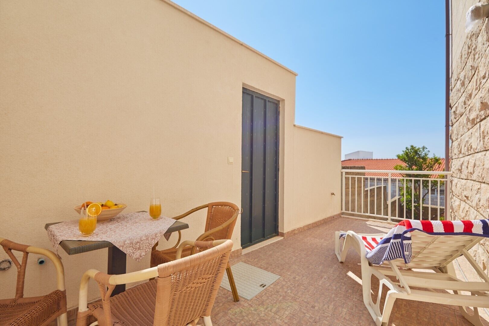 Un balcone con mobili in vimini, un tavolo con un bicchiere di succo d'arancia e vista sulla strada.