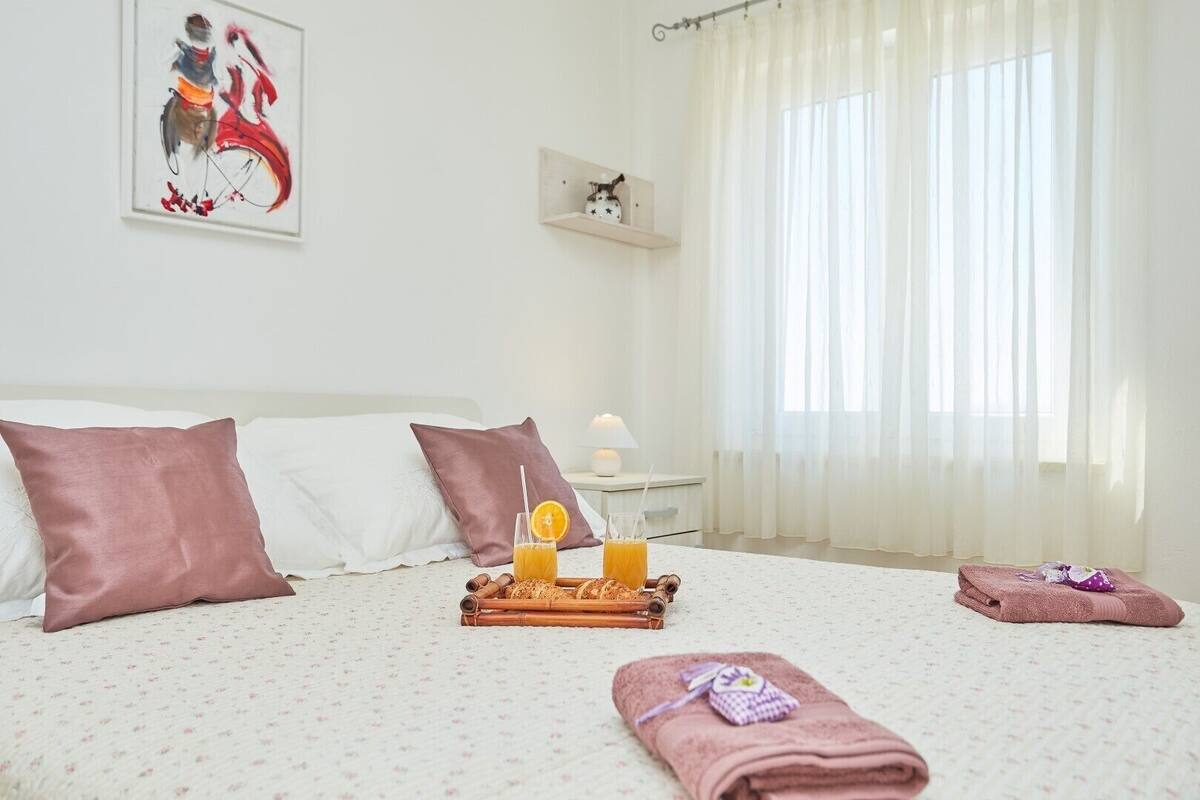 Een hotelkamer met een bed, een nachtkastje met een lamp, een raam met dunne gordijnen en een schilderij aan de muur.