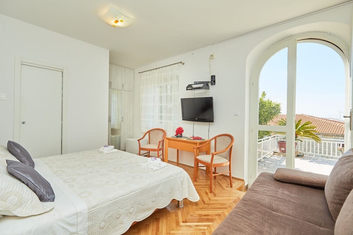 Een slaapkamer met een bed, een bureau, een televisie en uitzicht door een groot raam.