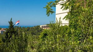 A coastal view with dense greenery, a flag, and a building in the background. - Villa Kate Dadic (Dubrovnik)