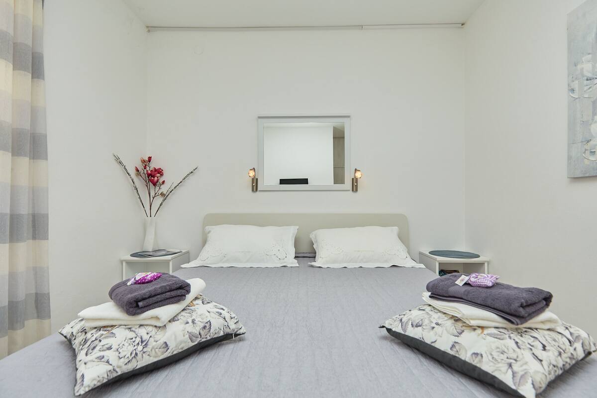 Een moderne slaapkamer met een groot bed, twee nachtkastjes, een spiegel en een vaas met bloemen.