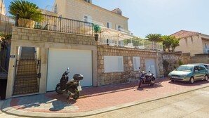 A two-story building with a stone facade, a balcony with a railing, and a parked scooter and car on the street. - Villa Kate Dadic (Dubrovnik)