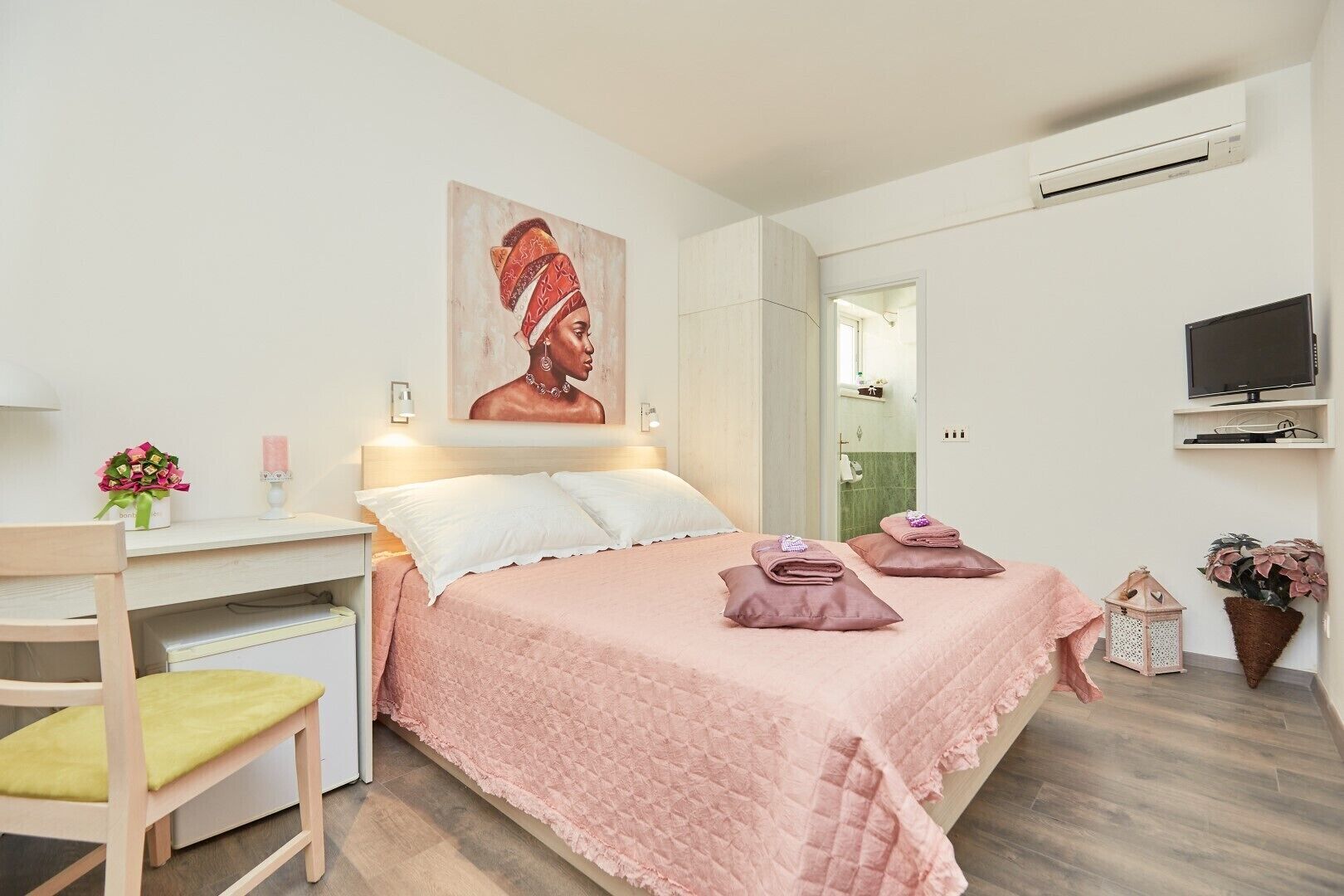Un dormitorio con cama, mesita de noche, silla, televisor y un cuadro en la pared.