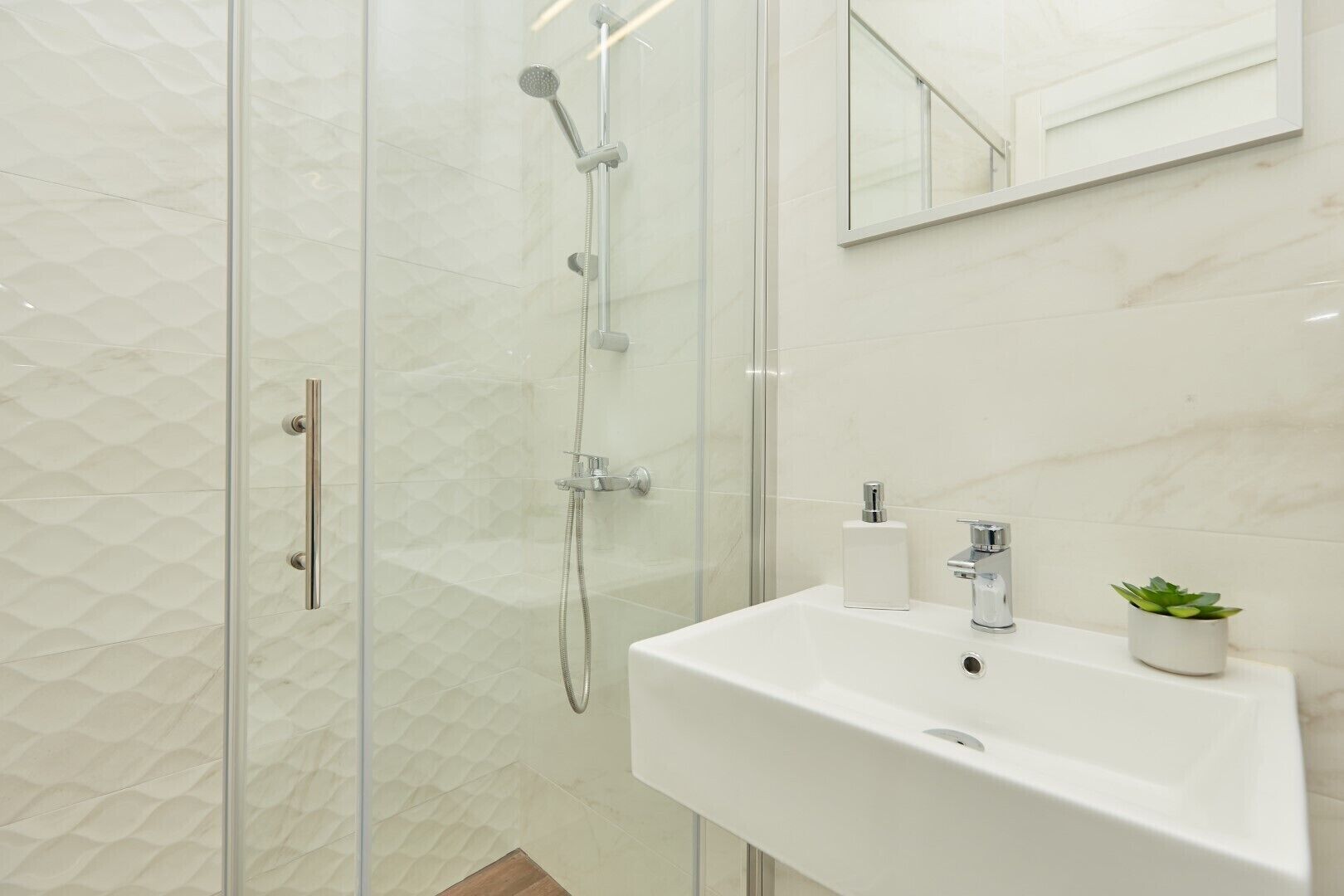 A modern bathroom with a glass-enclosed shower, a white sink, and a small potted plant.