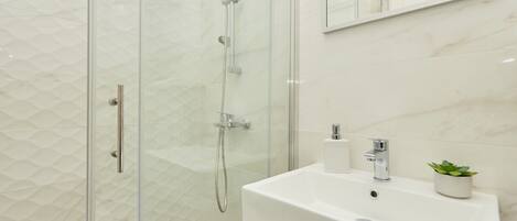 A modern bathroom with a glass-enclosed shower, a white sink, and a small potted plant.