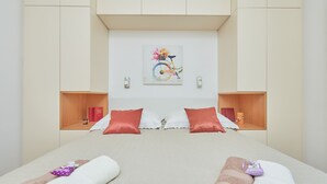 A modern hotel room with a large bed, two nightstands, a wall-mounted artwork, and a wooden shelf with books and a candle. - Villa Kate Dadic (Dubrovnik)