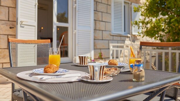 An outdoor dining area with a table set for breakfast, including croissants, orange juice, and a bottle of water. - Villa Kate Dadic (Dubrovnik)