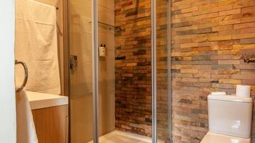 A modern bathroom with a glass-enclosed shower, wooden flooring, and a brick accent wall.