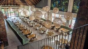 En rummelig restaurant med høje lofter, hængende runde lysarmaturer og store vinduer med udsigt til grønne områder.