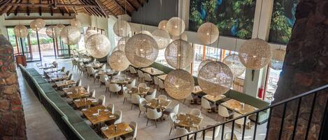 Un restaurante espacioso con techos altos, lámparas esféricas colgantes y amplias ventanas que ofrecen vistas a zonas verdes.