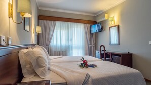 A hotel room with two beds, a TV mounted on the wall, a bedside table with a phone, and a window with curtains.