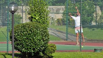 Tennisbane med en spiller i aktion, en bænk og en lygtepæl.