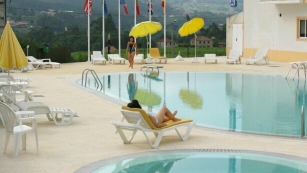 A pool area with lounge chairs and umbrellas, flags, and a view of the surrounding landscape.