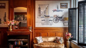 A cozy room with a fireplace, a sofa, a bookshelf, and a large window with shutters. - Hotel Mansion (Amsterdam)