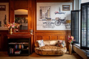 Une pièce chaleureuse avec une cheminée, un canapé, une bibliothèque et une grande fenêtre avec des volets.