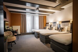 Habitación de hotel con una cama grande, un escritorio, una silla y un ventanal con cortinas.
