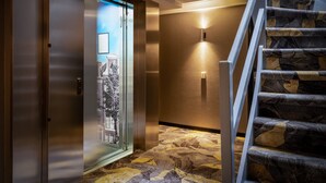 A modern elevator with a glass door, a carpeted floor, and a staircase with patterned steps. - Hotel Mansion (Amsterdam)