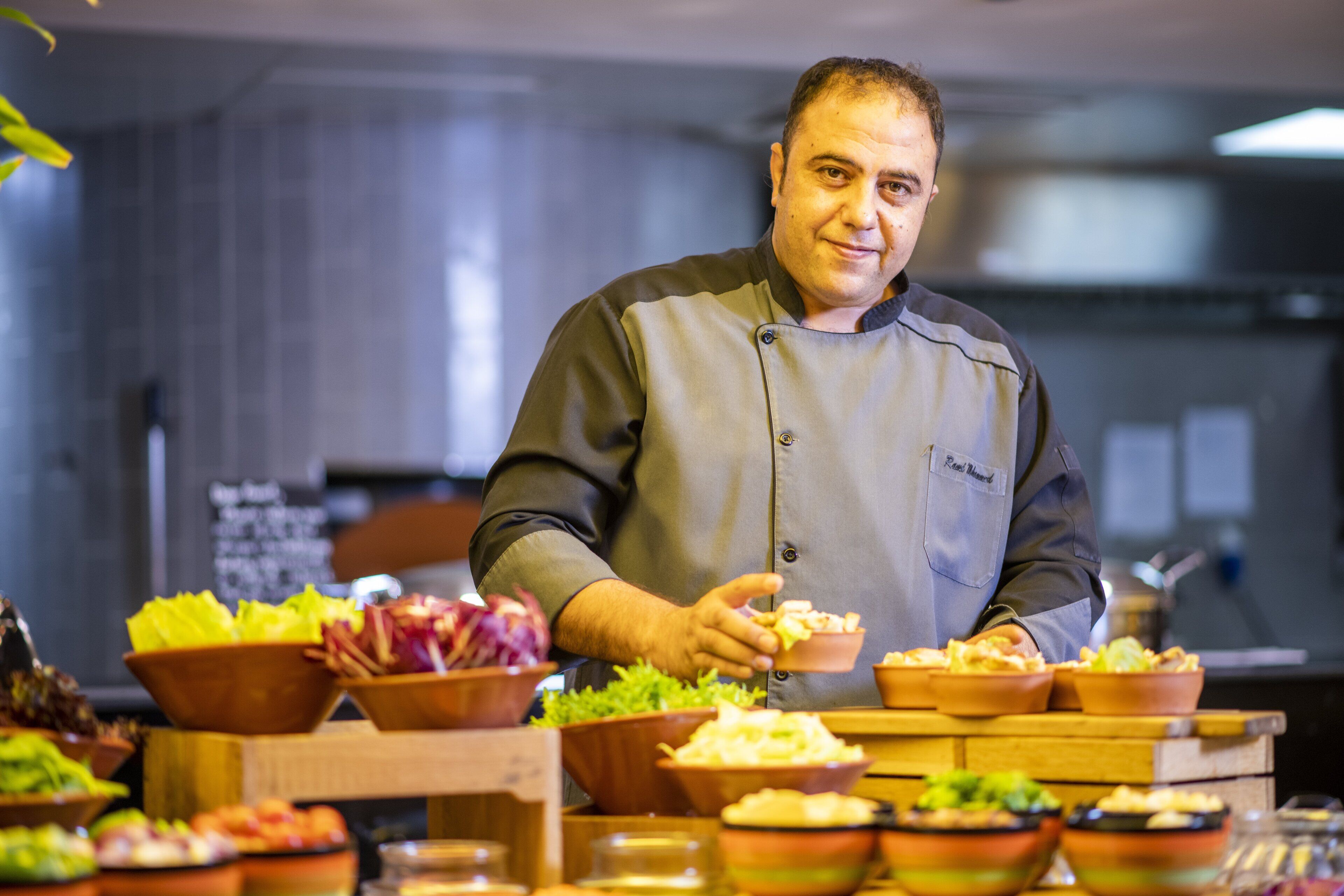A chef in a kitchen preparing food with various ingredients and dishes visible.