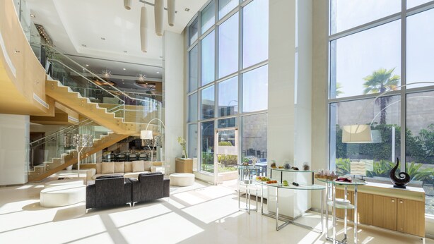 A spacious, modern living area with a staircase, large windows, and a kitchen area.