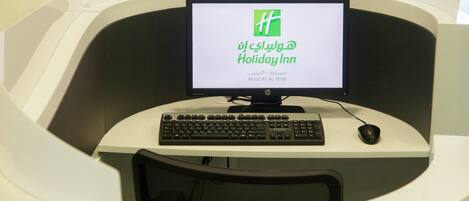 Un equipo de computadora con un monitor que muestra 'Holiday Inn' en varios idiomas, un teclado y un ratón sobre un escritorio blanco.
