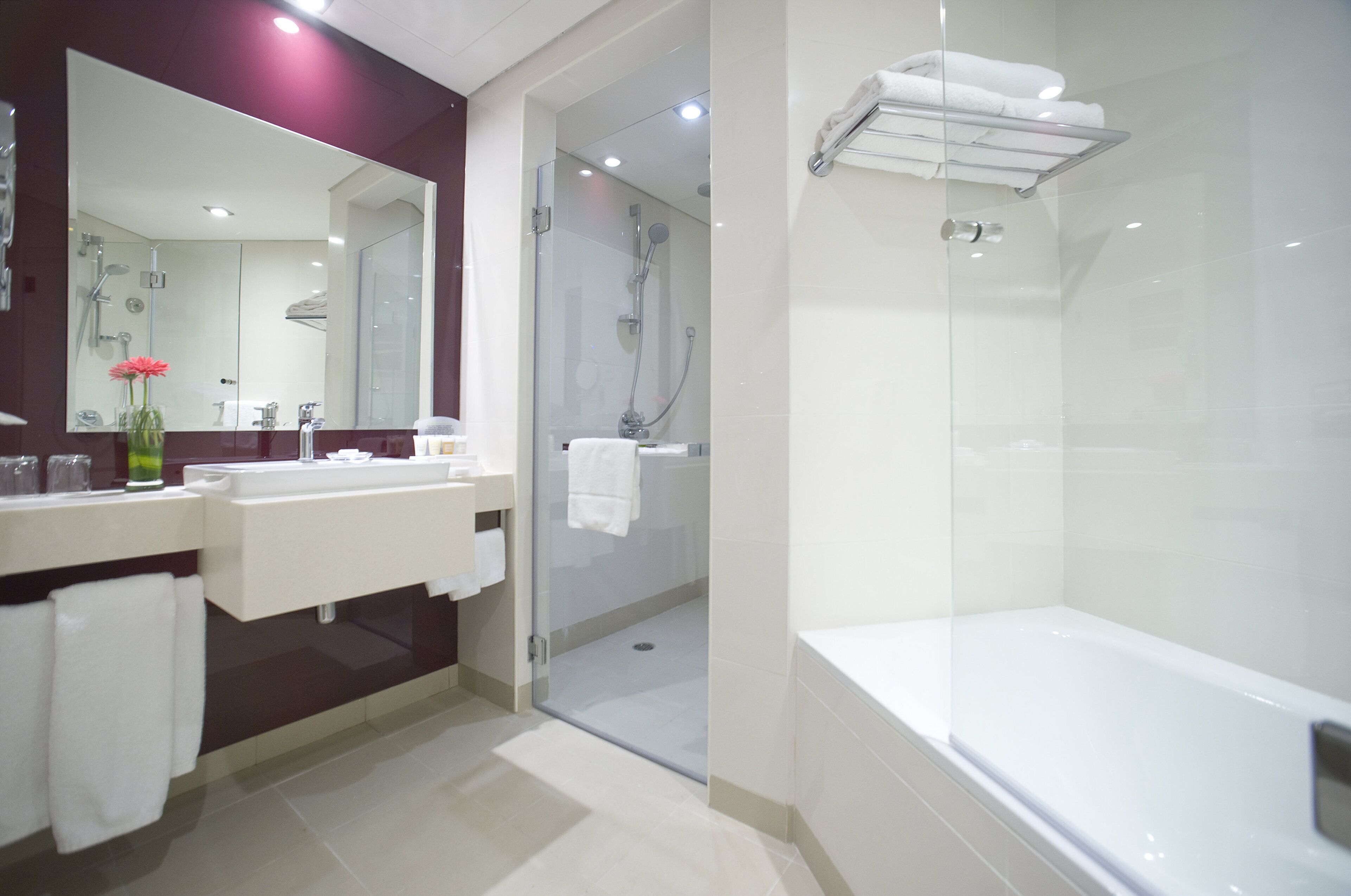 A modern bathroom with a glass-enclosed shower, a white bathtub, and a vanity with a mirror.