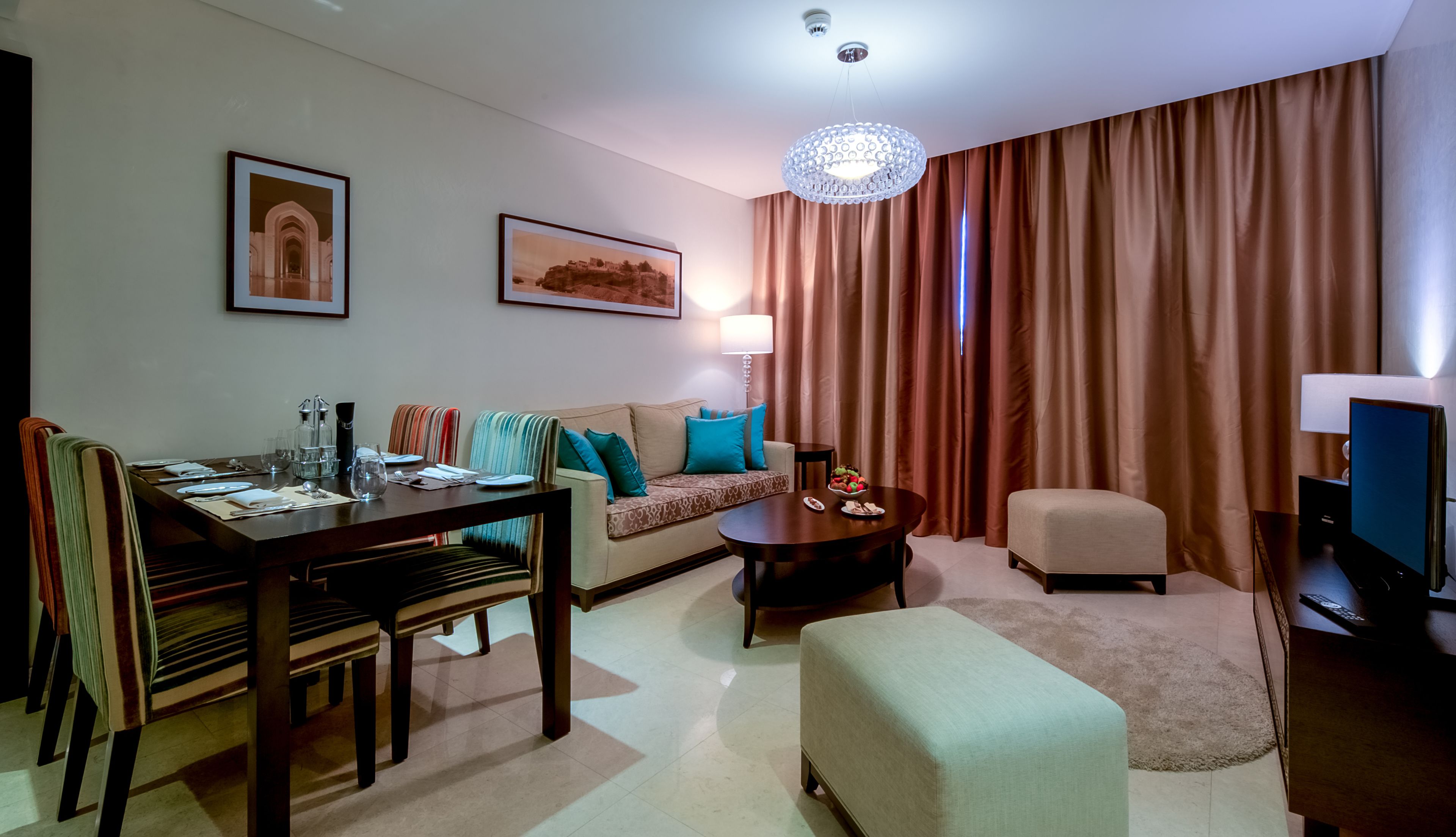 Una sala moderna con comedor, un sofá con cojines de colores, una mesa de centro, televisor y un ventanal con cortinas.