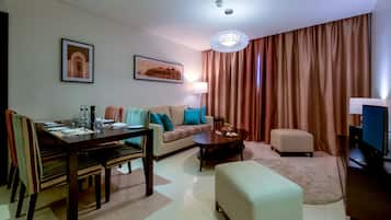 Una sala moderna con comedor, un sofá con cojines de colores, una mesa de centro, televisor y un ventanal con cortinas.