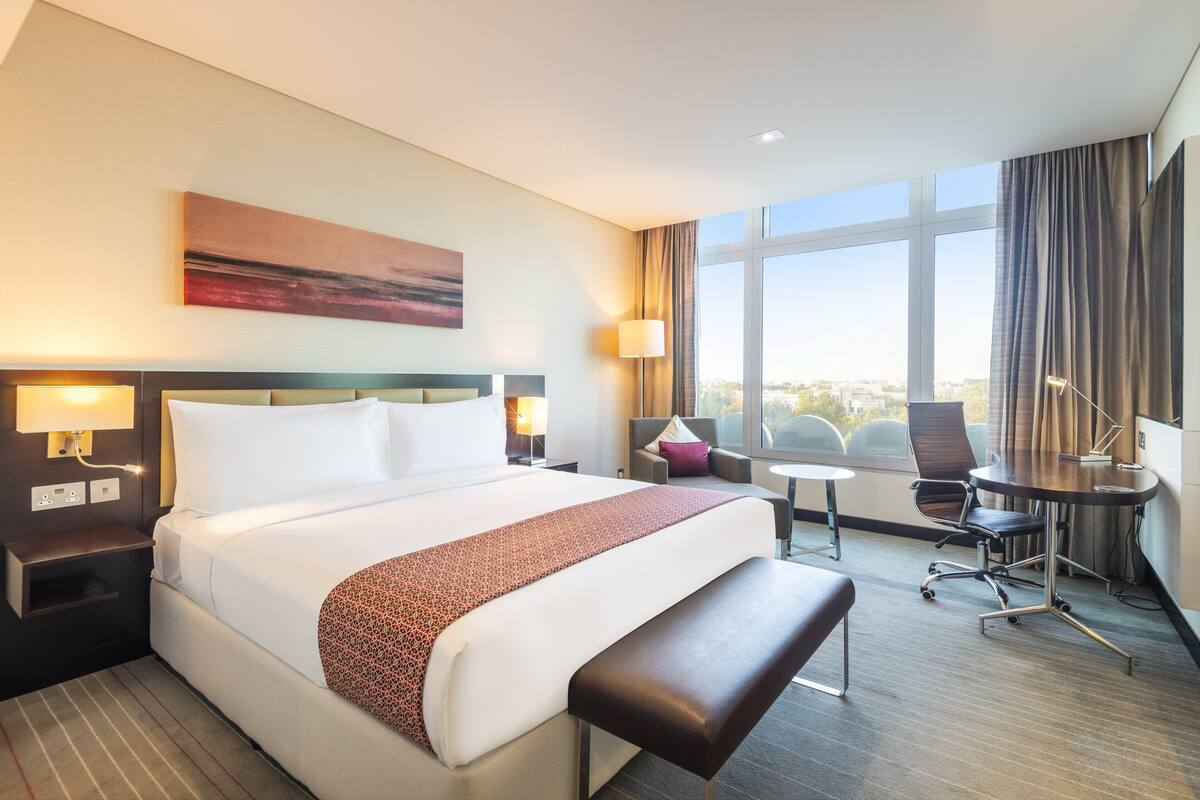 A hotel room with a large bed, a desk, a chair, and a view of the city.