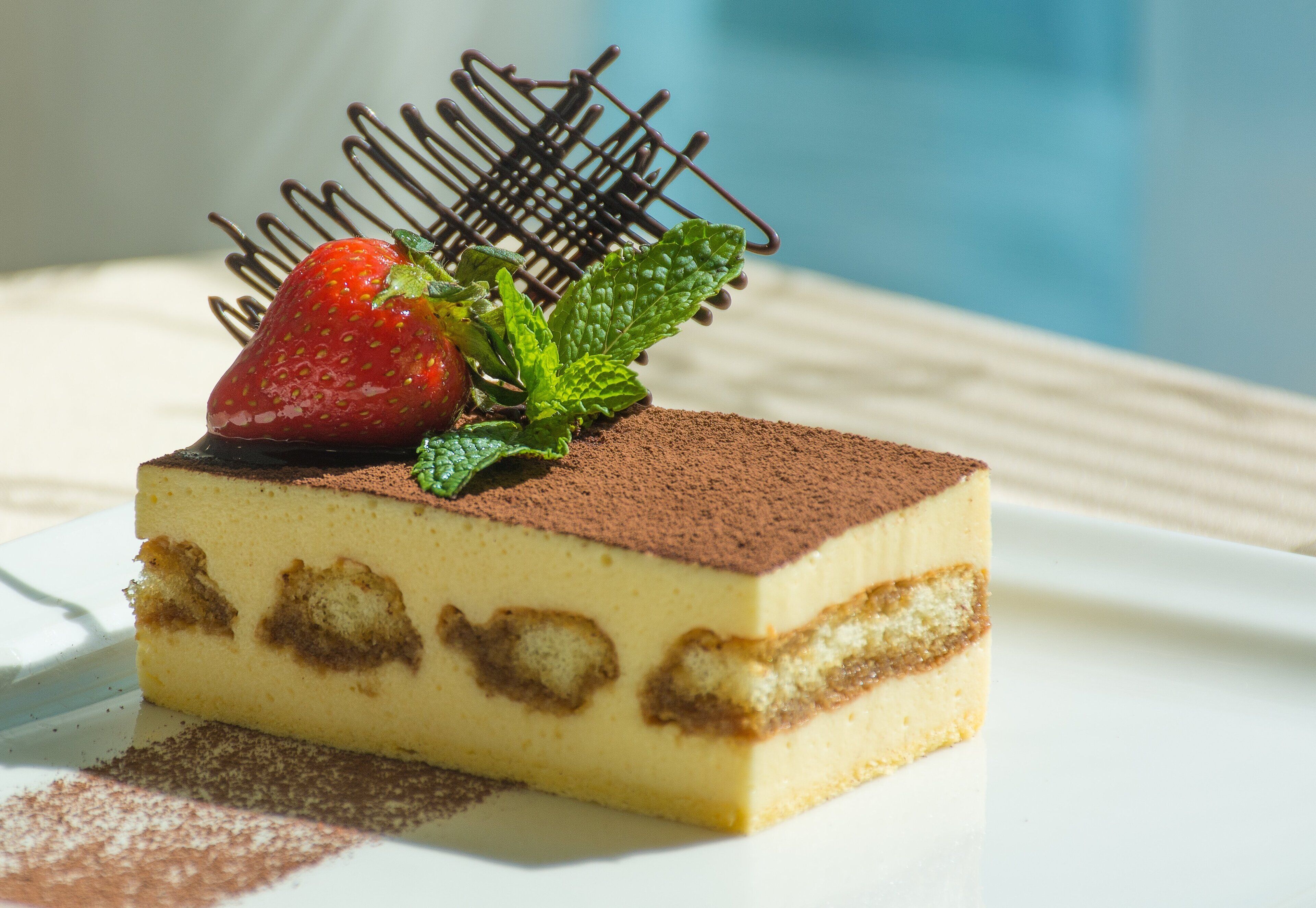 Una porción de postre en capas, adornada con fresa y menta, sobre un plato blanco.