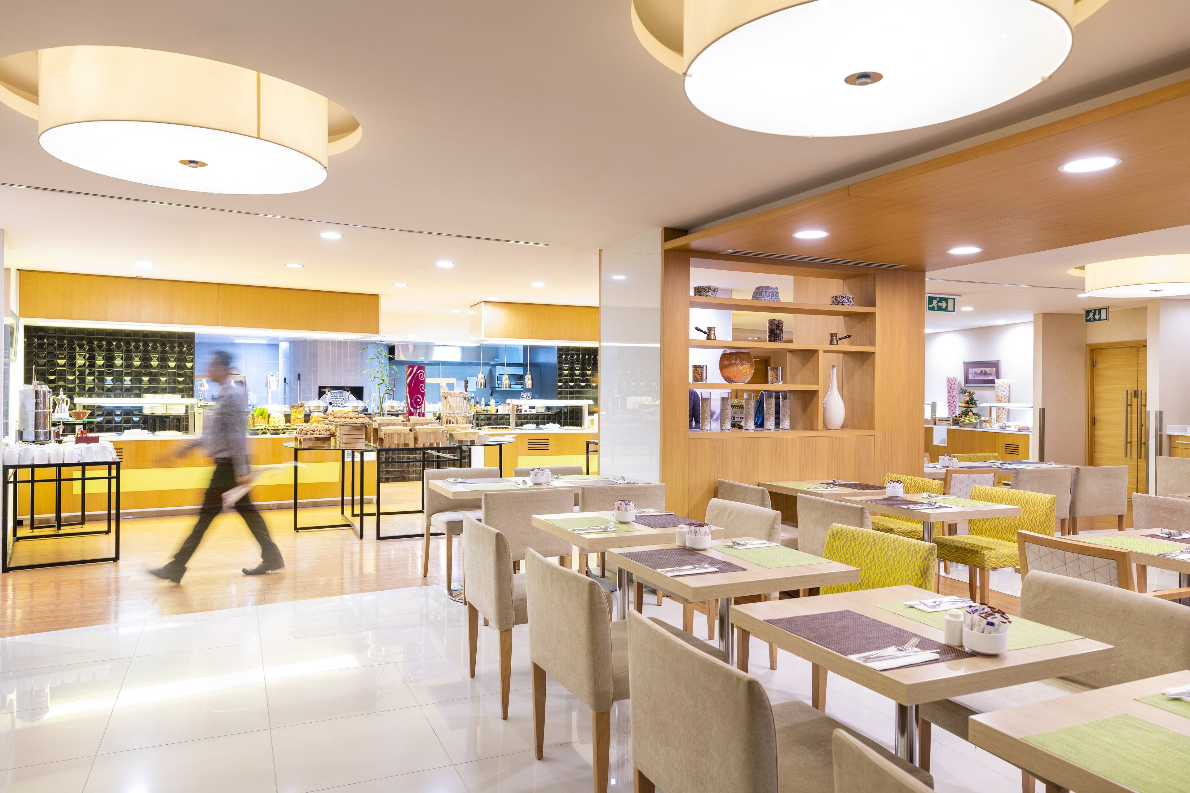 A modern restaurant with a bright interior, multiple dining areas, and a visible kitchen in the background.